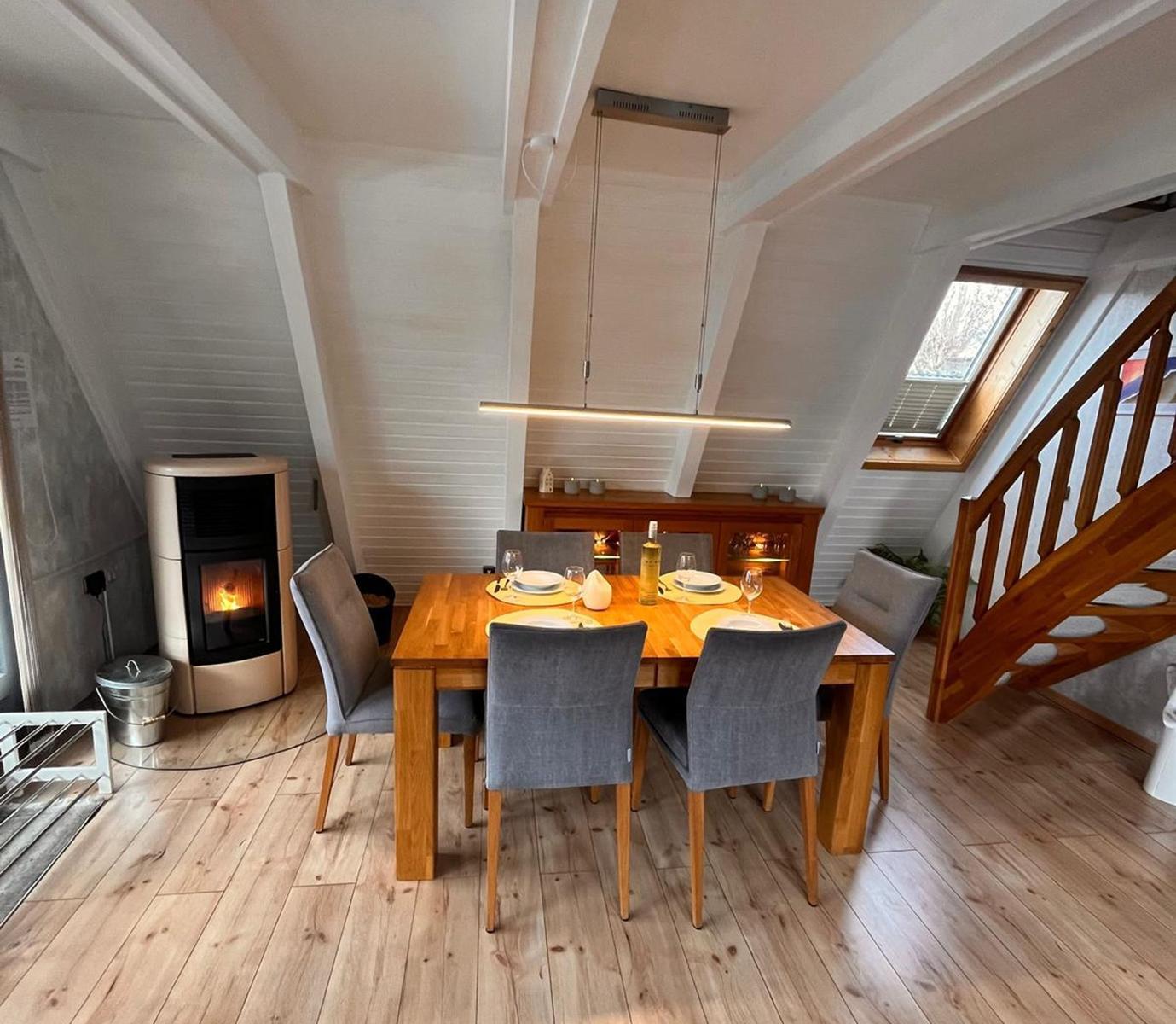 Esszimmer mit Holztisch, Stühlen und Kaminofen unter Dachschrägen.