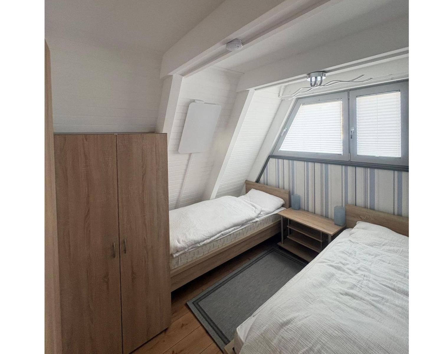 Zimmer mit zwei Betten, Kleiderschrank und Fenster mit Jalousien.