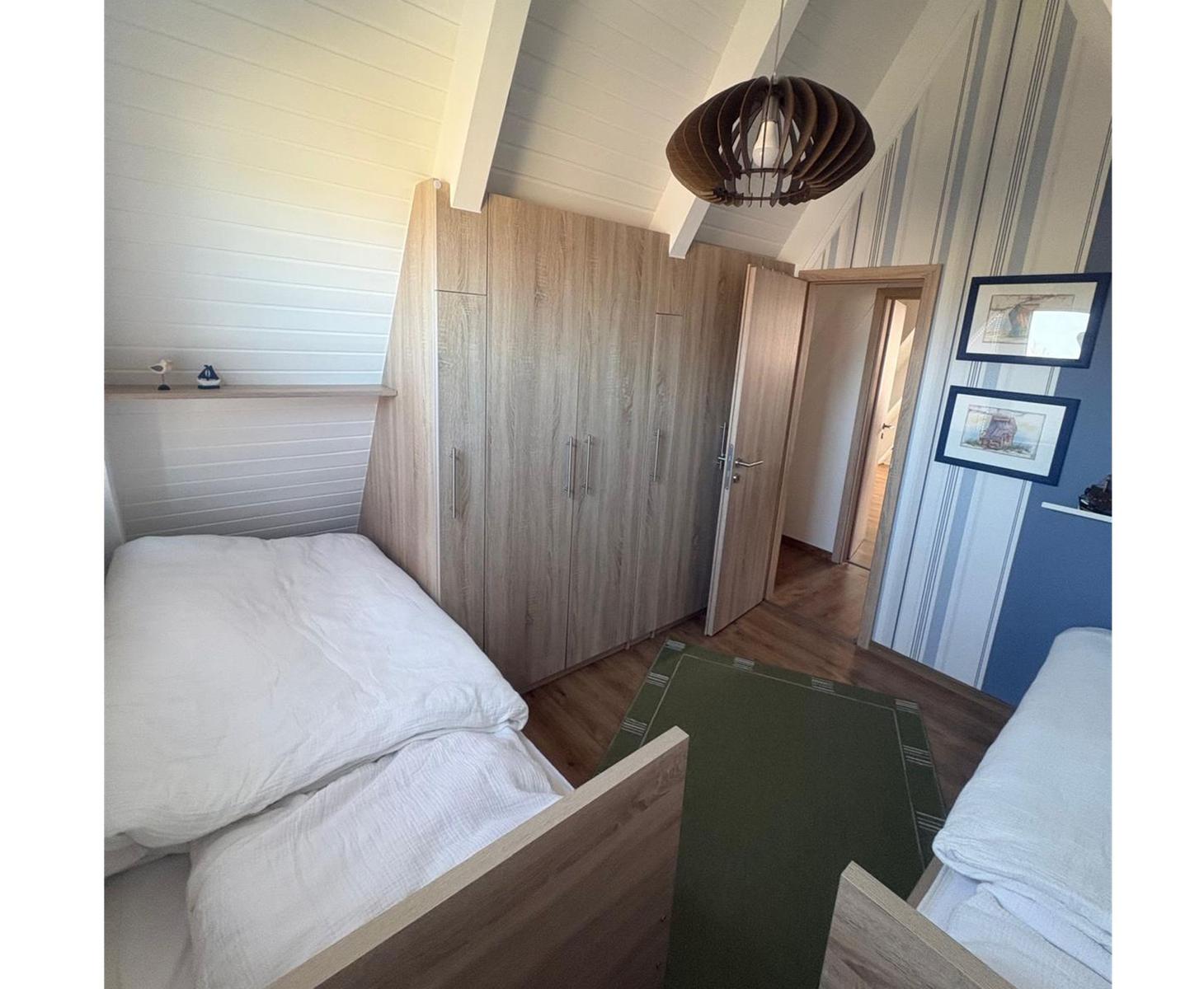 Zimmer mit zwei Betten, Kleiderschrank und Decke unter Dachschrägen.