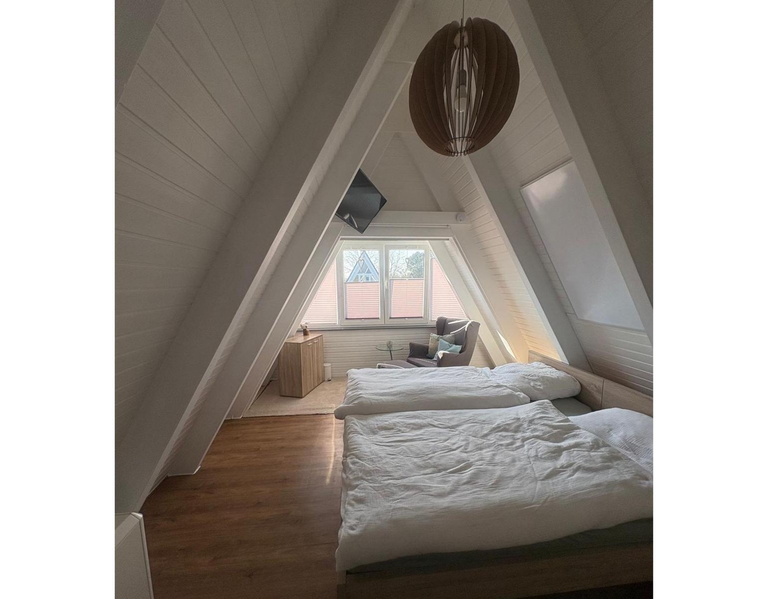 Schlafzimmer mit Dachschrägen, Bett, Sessel und Fenster.