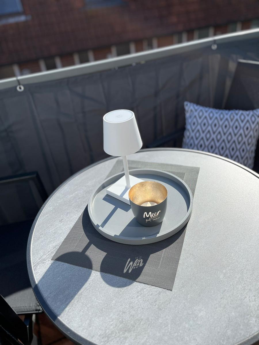 Runder Tisch mit Laterne und Tasse auf Balkon. Hintergrund: Sitzgelegenheit mit Kissen.
