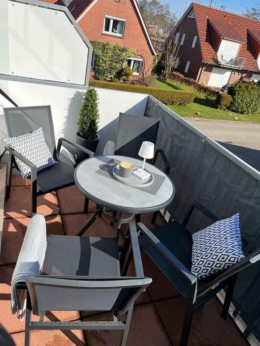 Terrasse mit Tisch und drei Stühlen, Pflanze und Blick auf Wohnhäuser.