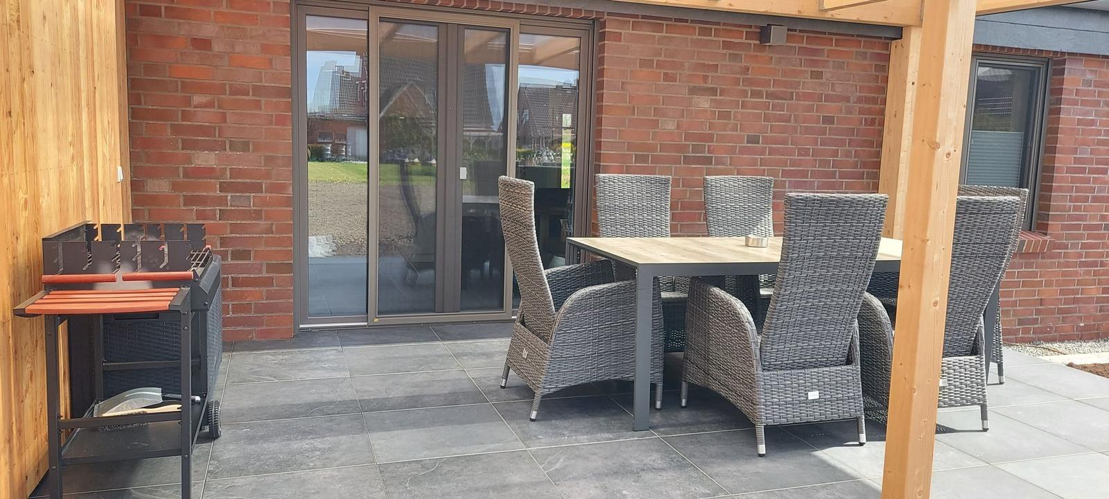 Terrace with dining table, chairs, and grill. Background: red brick wall and glass doors.