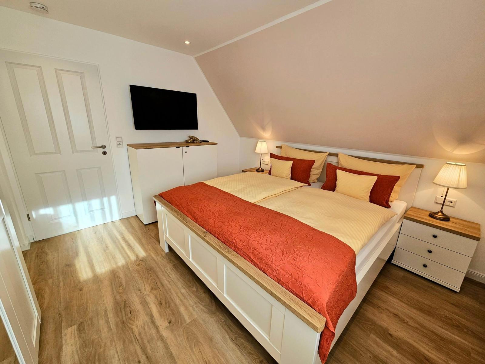 Schlafzimmer mit Doppelbett, Nachttischen und Fernseher an der Wand.