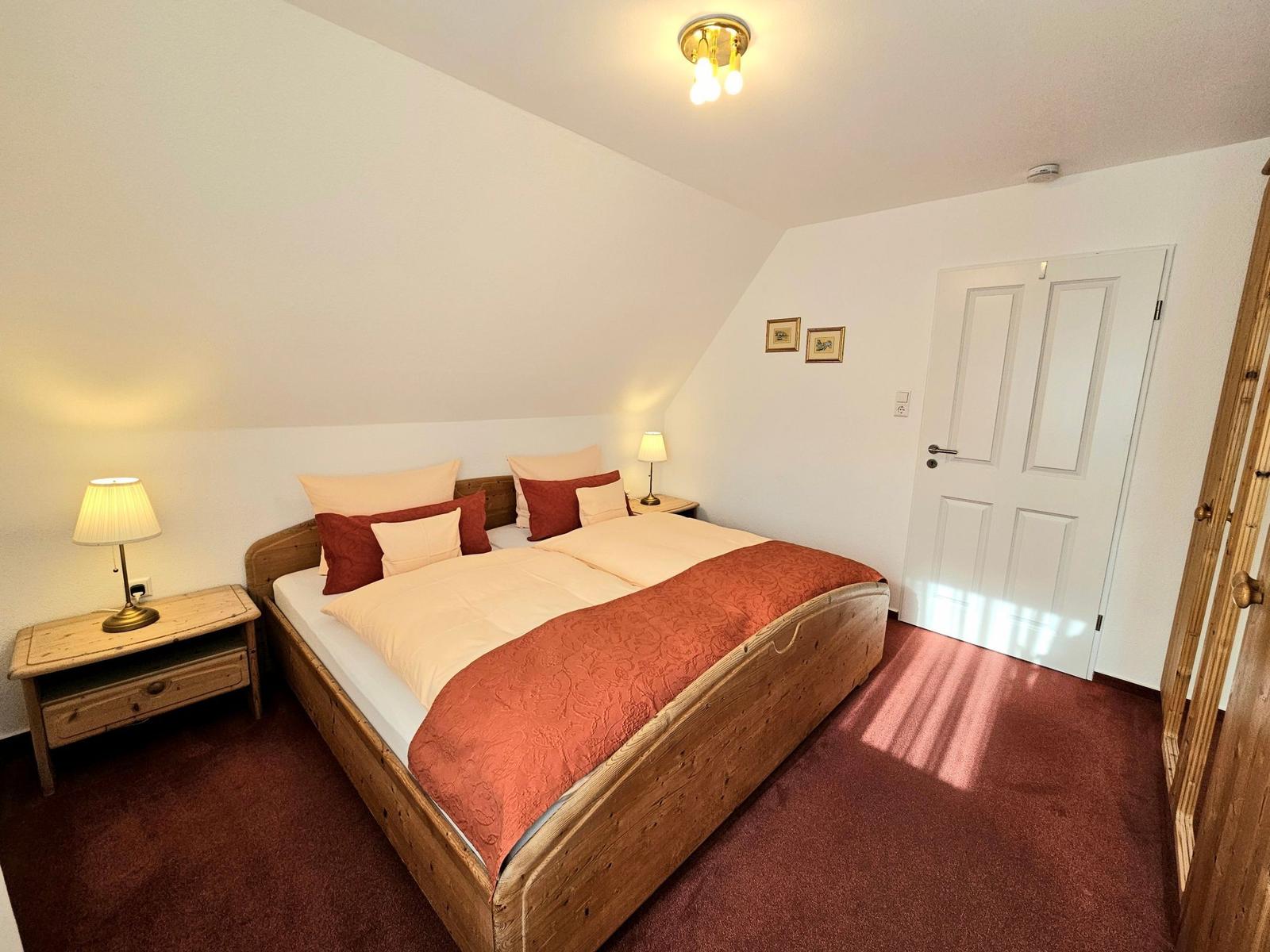 Schlafzimmer mit Holzbett, zwei Nachttischen und einer Tür.