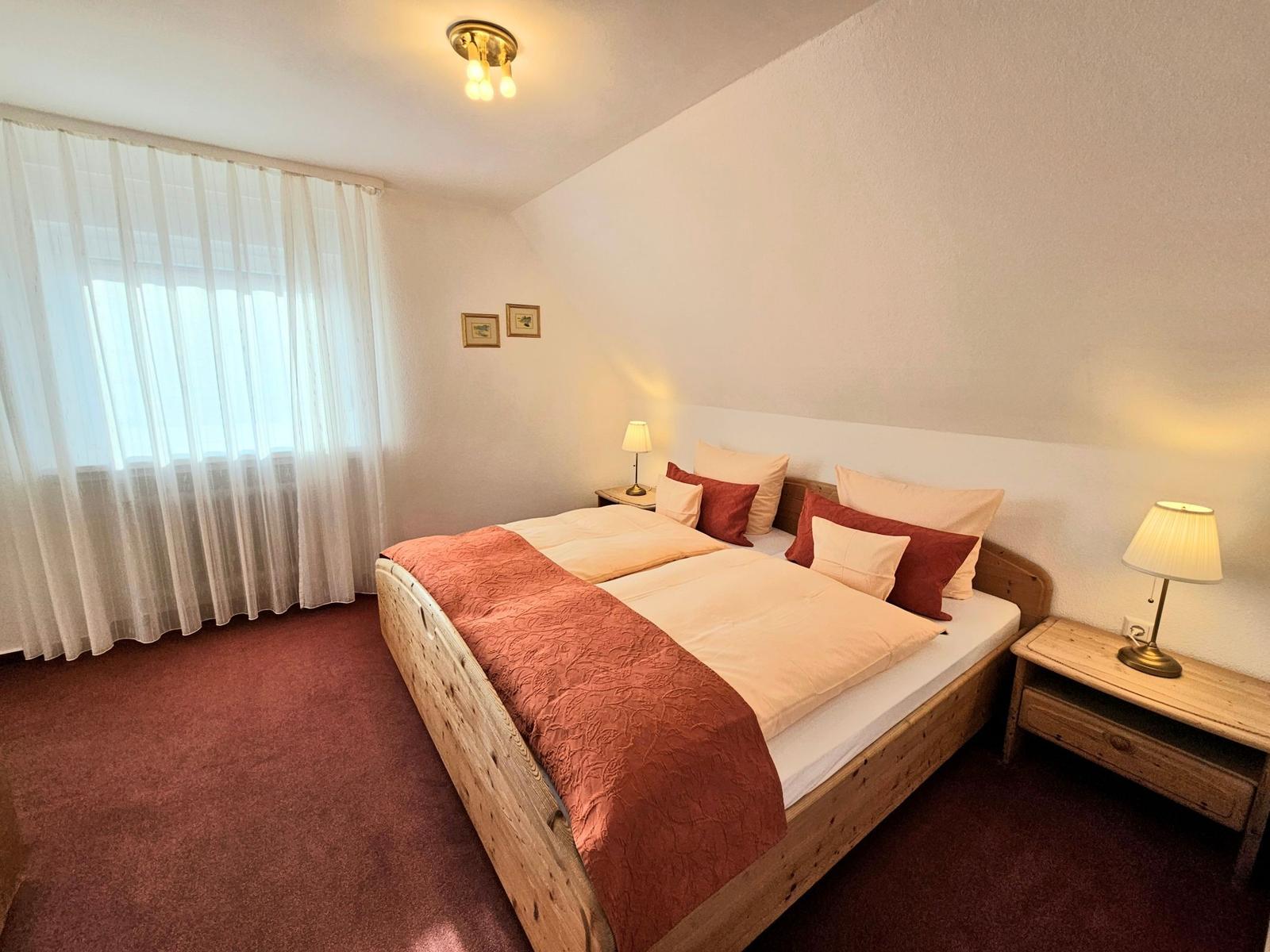 Schlafzimmer mit Holzbett, zwei Nachttischen und Vorhang an Fenster.