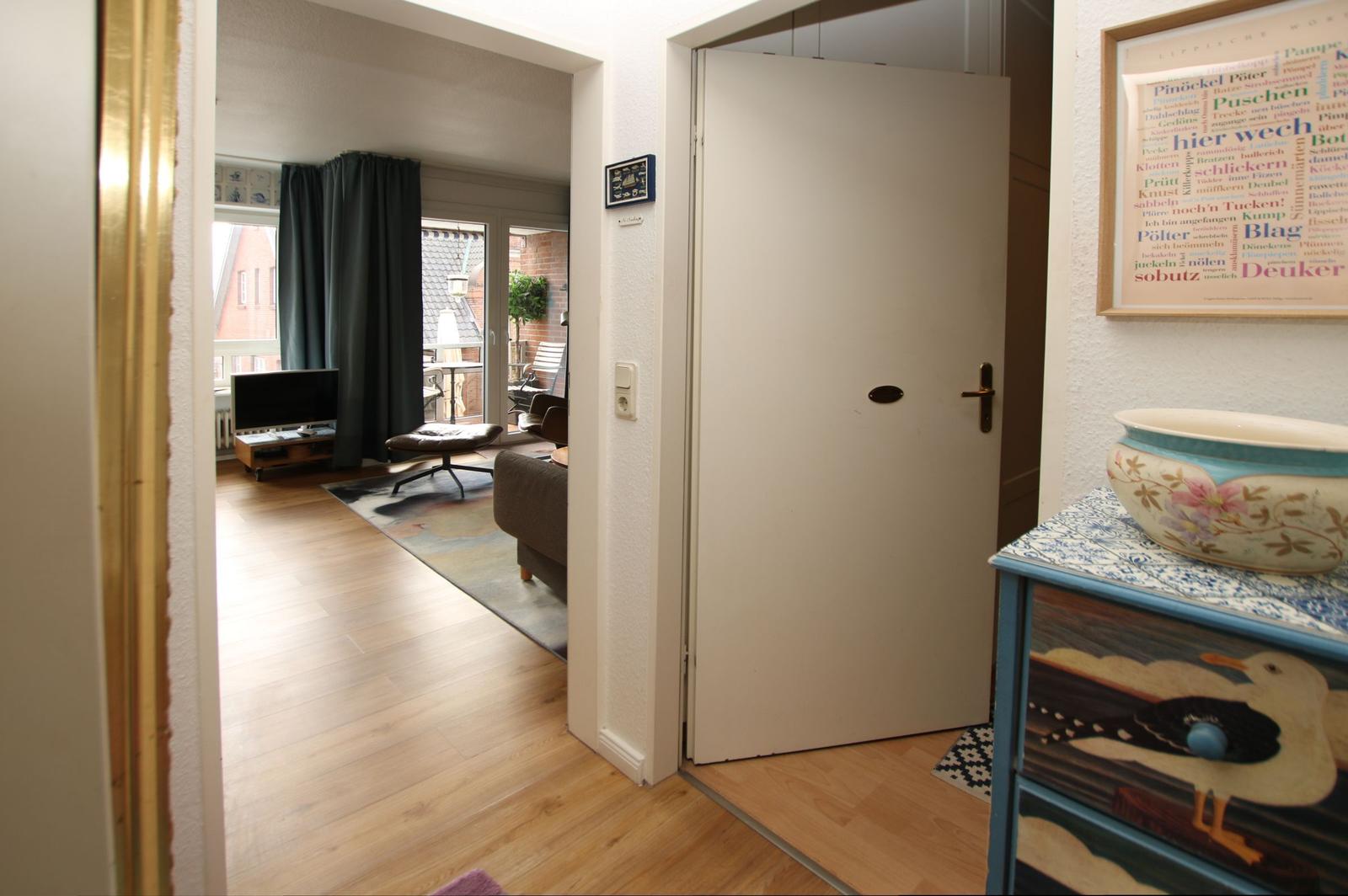 Eingangsbereich mit Tür und Dekorationsstück. Durchgang in Wohnzimmer mit TV und Balkon.