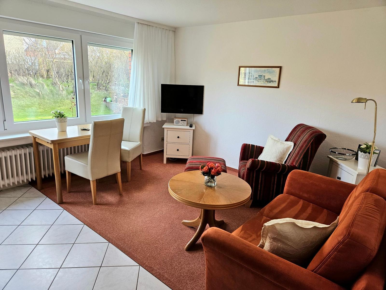 Living room with sofa, armchair, table, and TV. Window with view of garden.
