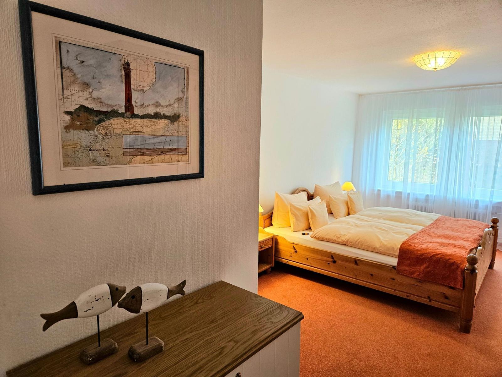 Bedroom with wooden bed, window, and wall art with lighthouse.