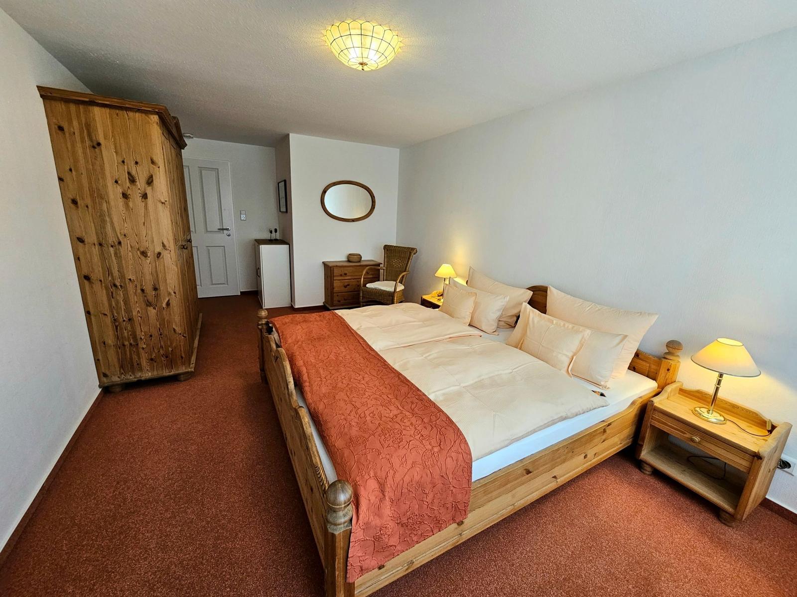 Bedroom with wooden bed, wardrobe, and nightstand. Carpeted floor and ceiling light.