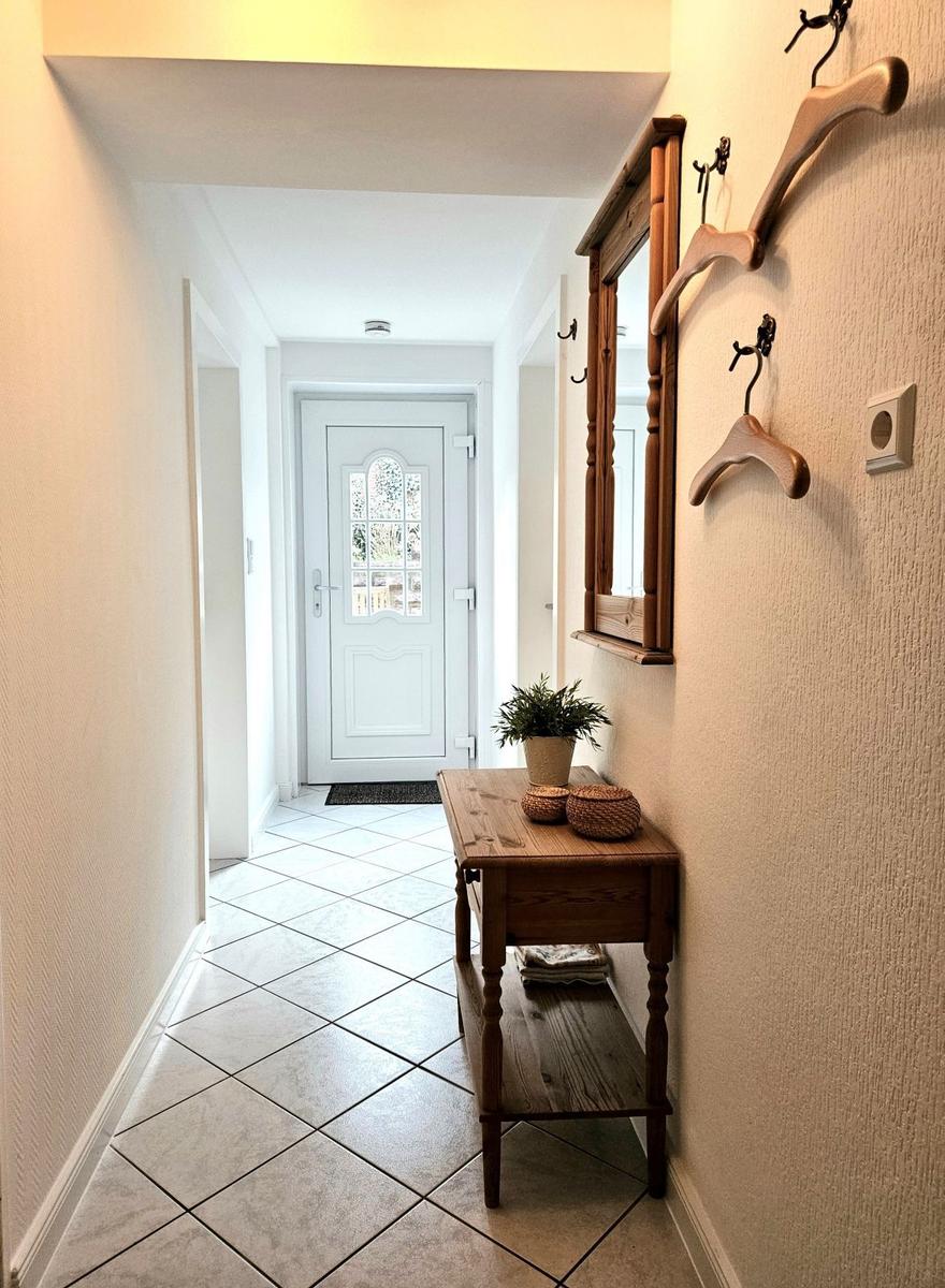 Hallway with wooden bench, mirror, and hooks on wall. Door at the back.