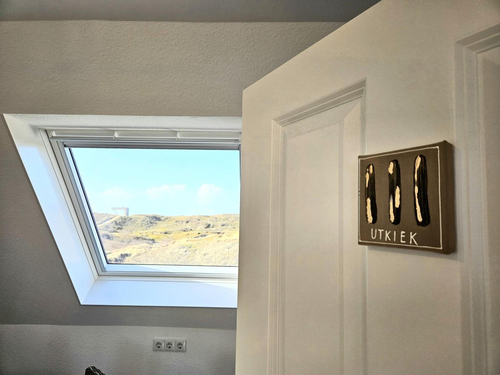 Dachfenster mit Blick auf Hügel. Tür mit Schild UTKIEK.