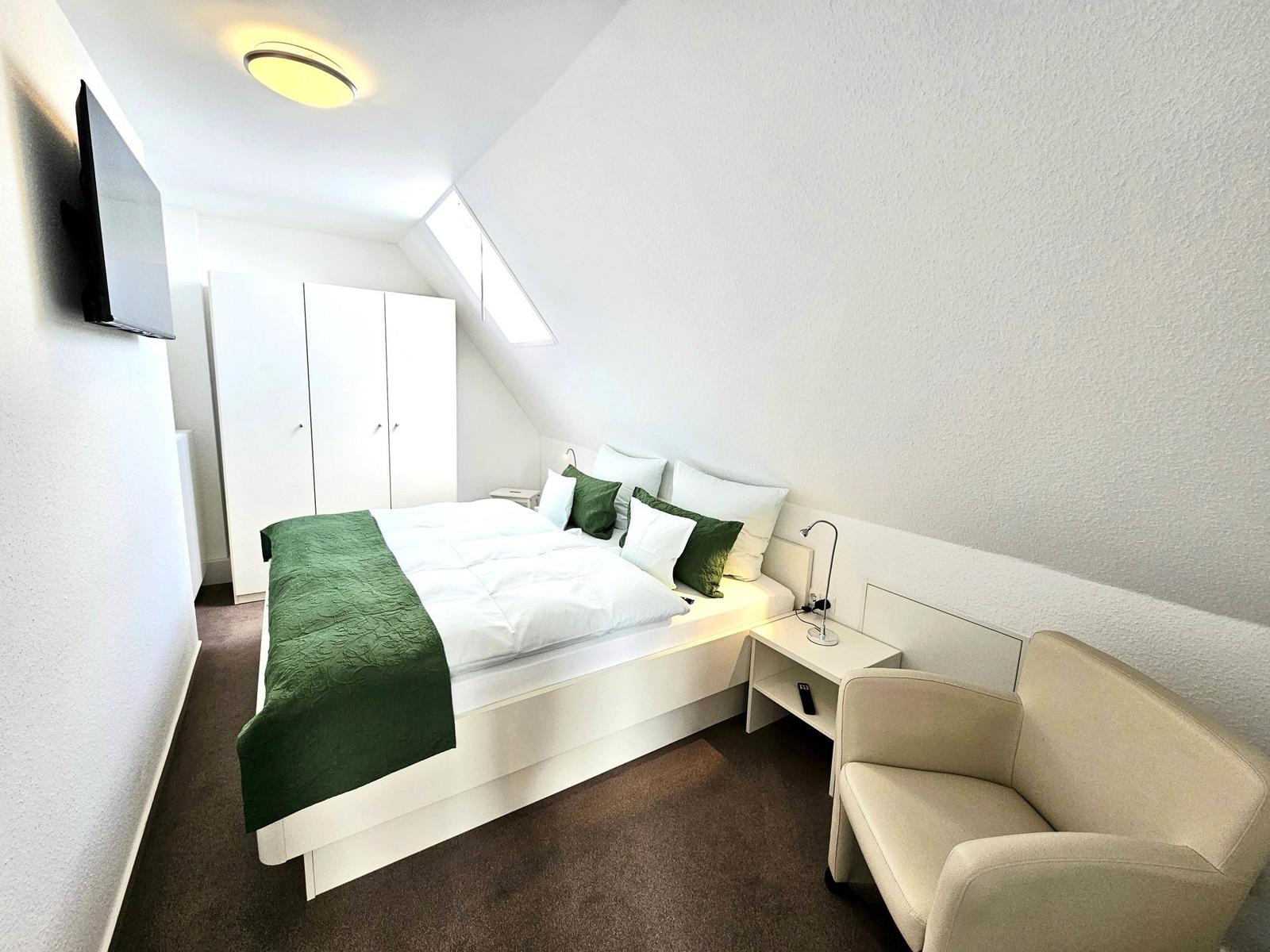 Schlafzimmer mit Bett, Kleiderschrank, TV und Sessel unter Dachschrägen.