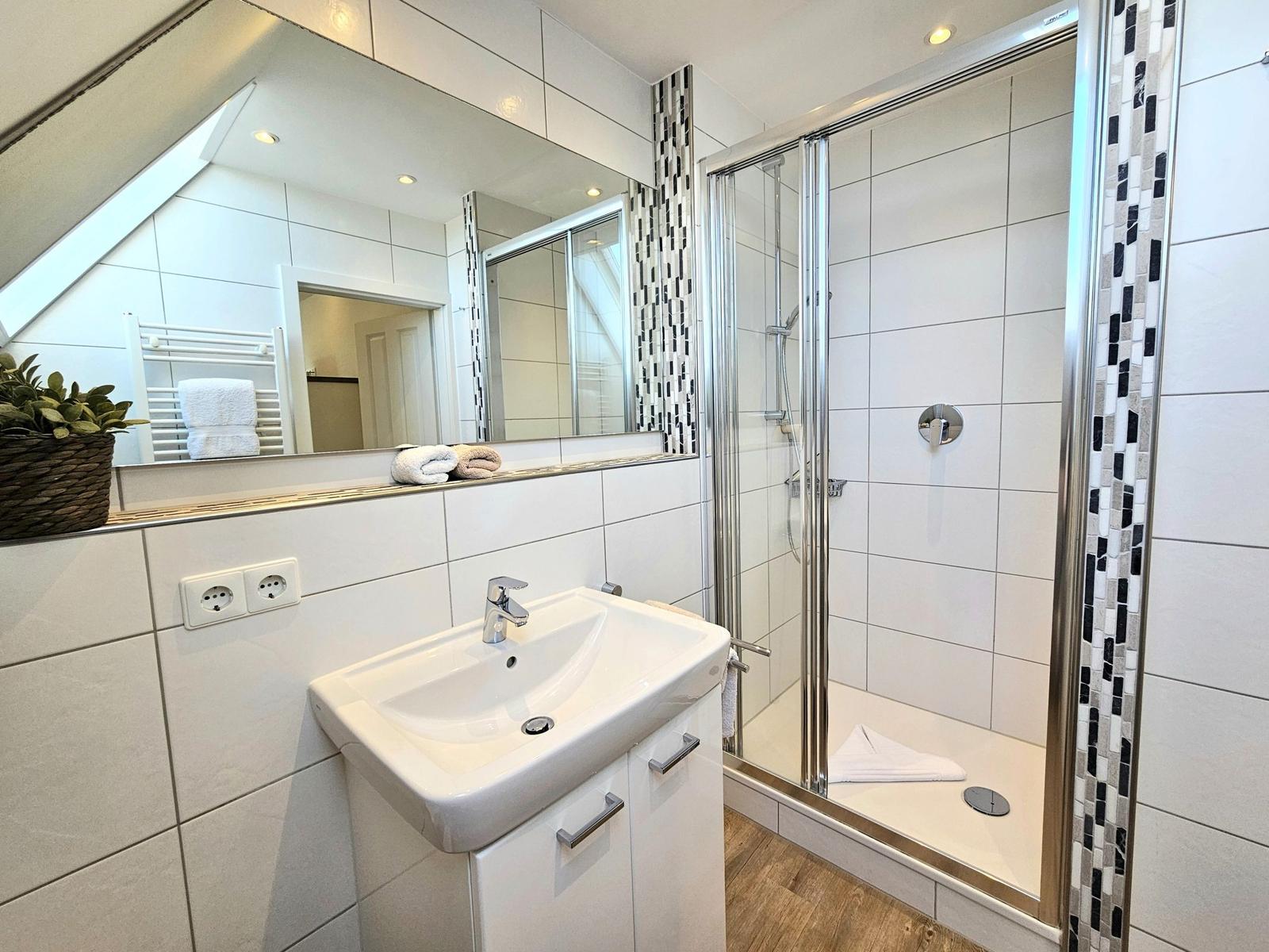 Badezimmer mit Dusche, Waschbecken und Spiegel