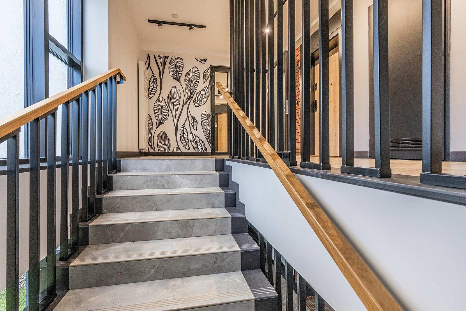 Treppe mit grauen Stufen und Holzgeländer führt zu einer Wand mit Blattmotiv.