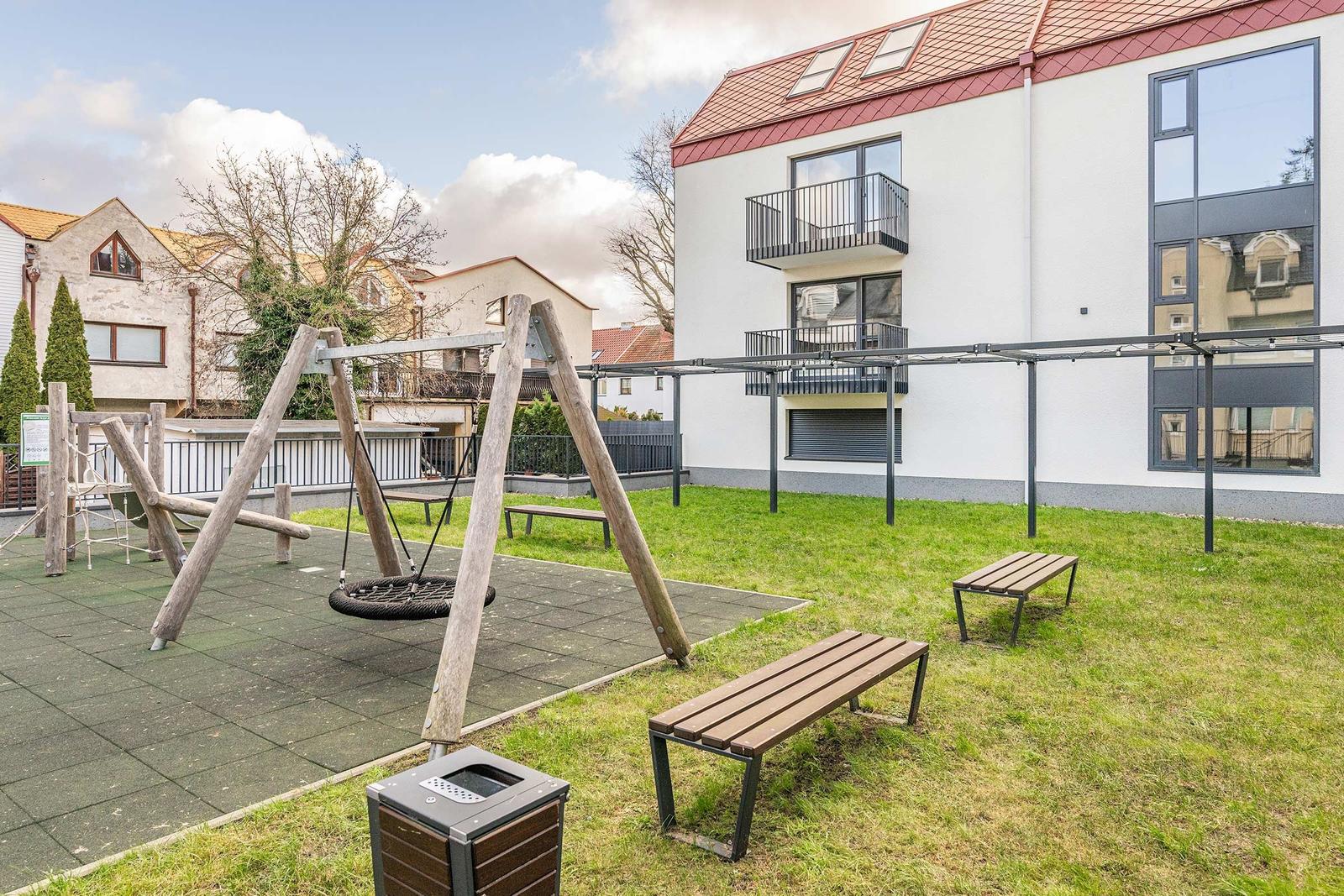 Hinterhof mit Spielplatz, Bänken und modernem Gebäude.