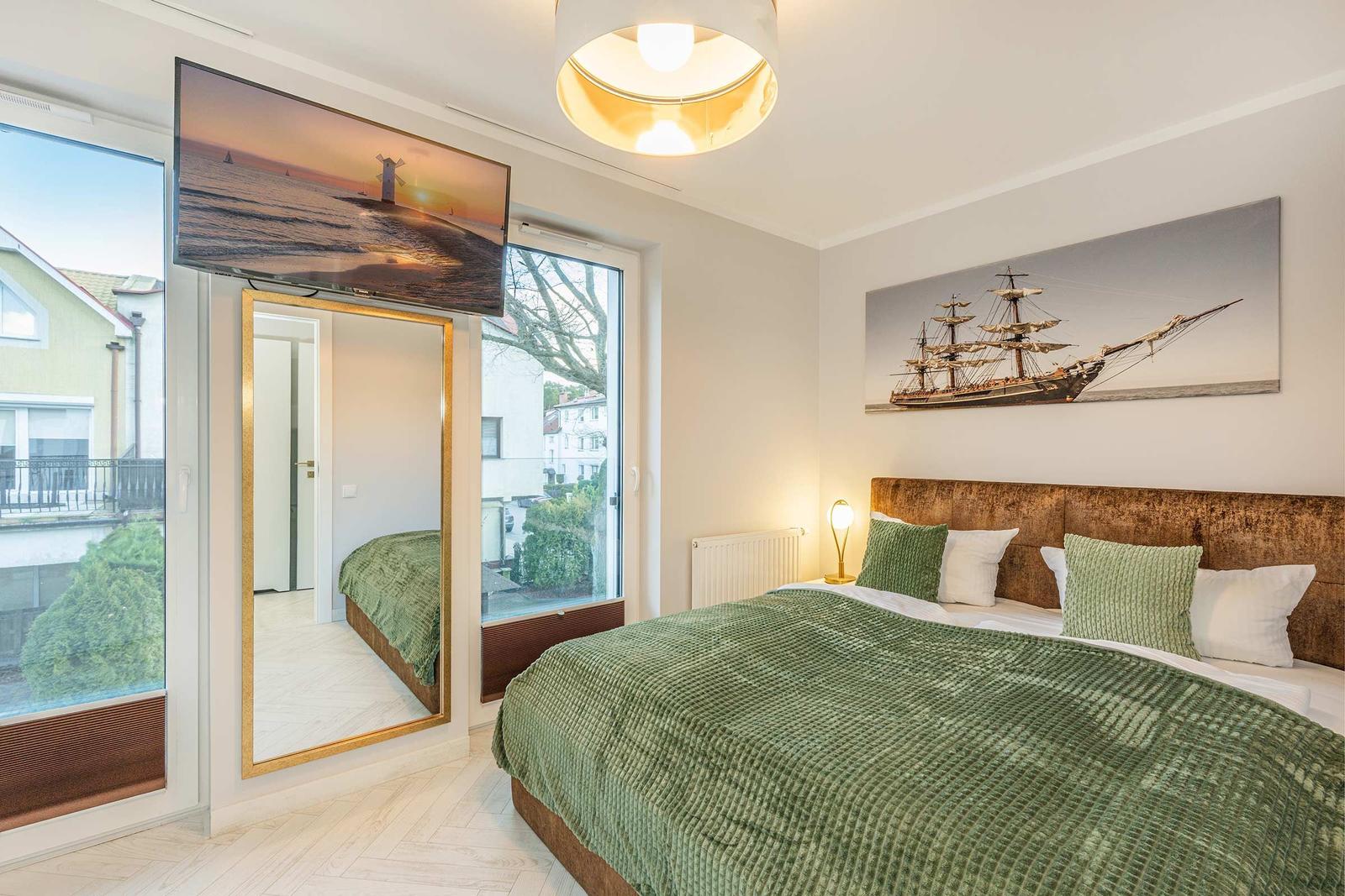 Schlafzimmer mit Bett, Fenster, Spiegel und Wandbildern.