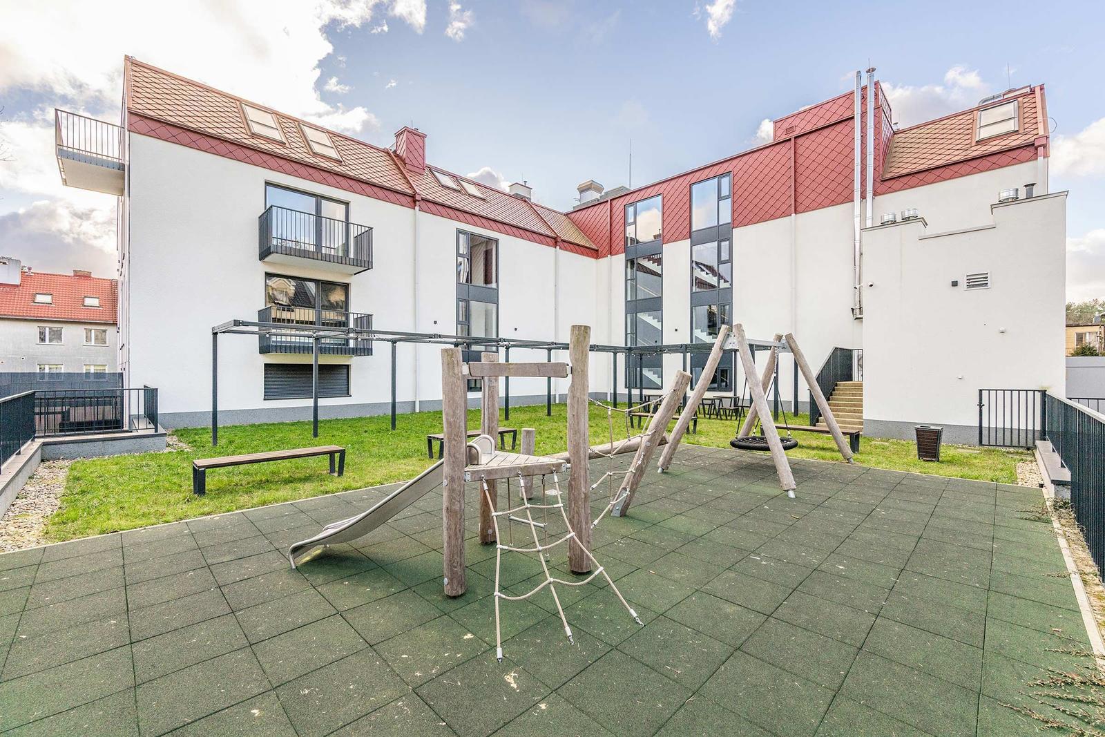 Hinterhof mit Spielplatz, Grünfläche und modernem Mehrfamilienhaus mit Balkonen.