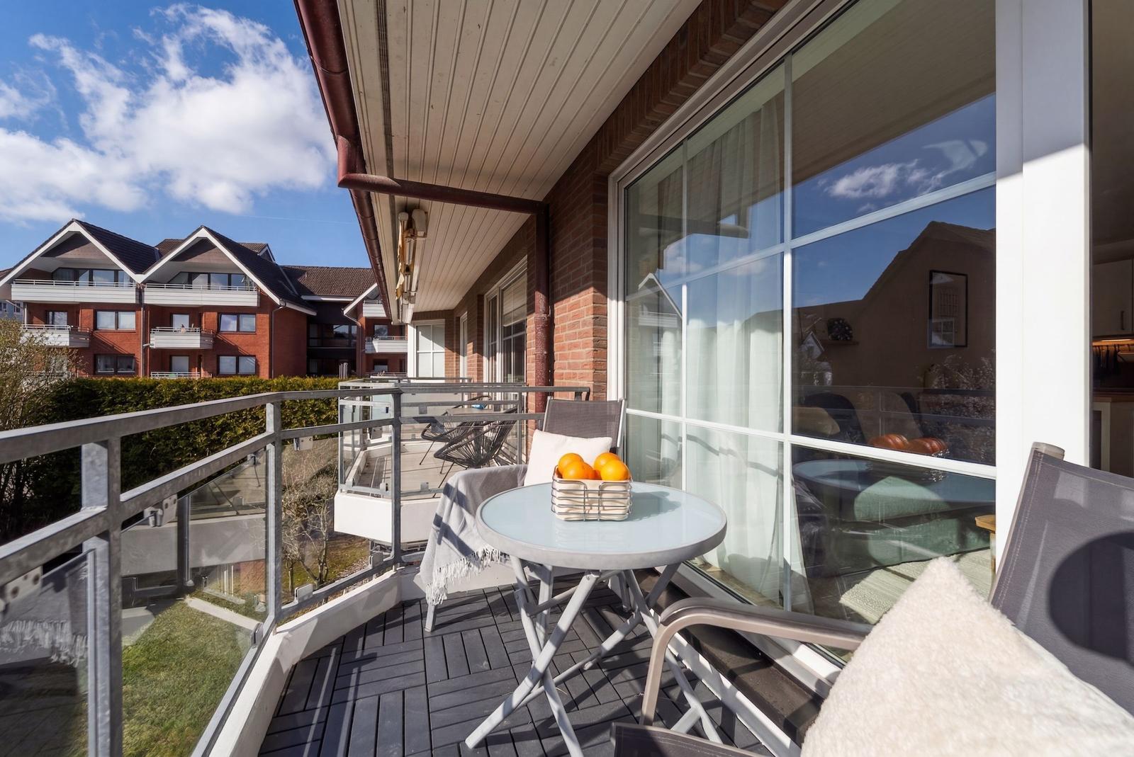 Terrasse mit Tisch, Stühlen und Korb mit Orangen. Blick auf Wohnhäuser und Himmel.