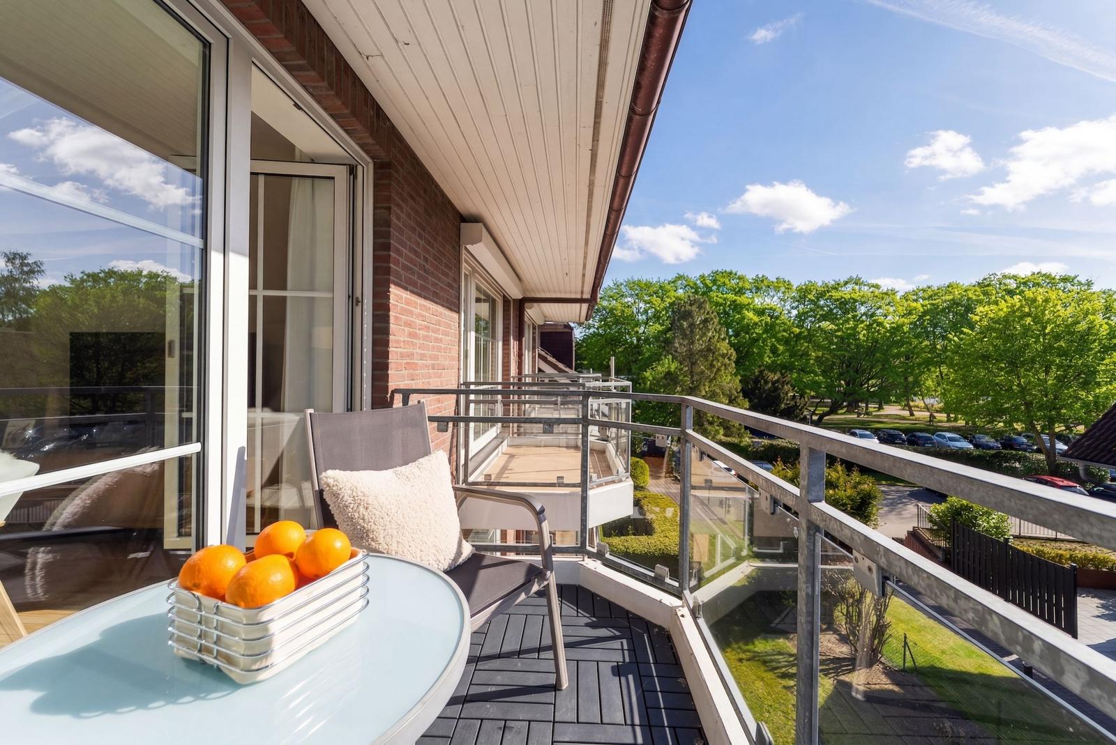 Terrasse mit Sitzgelegenheit und Obstschale. Blick auf grüne Bäume und Parkplatz.