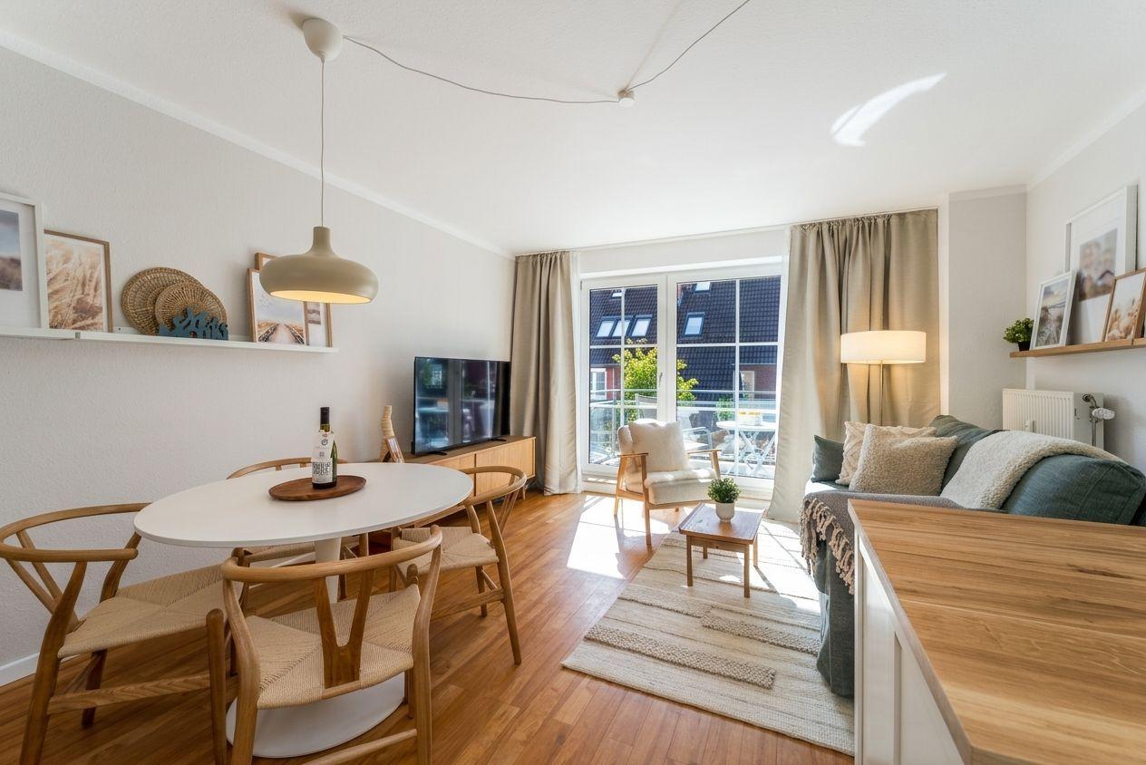 Wohn- und Essbereich mit Holzboden, Sofa, Esstisch und Balkonansicht.