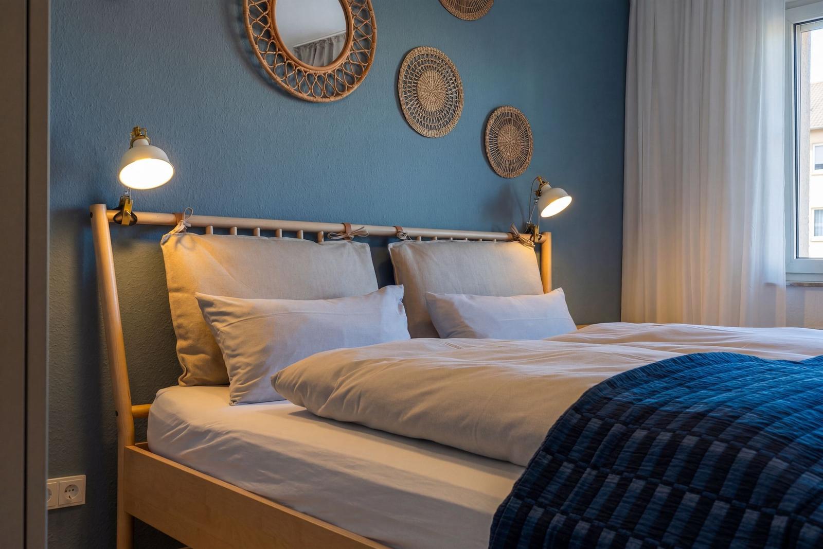 Ein Bett mit weißer Bettwäsche und blauer Decke vor blauer Wand mit Wanddekoration.