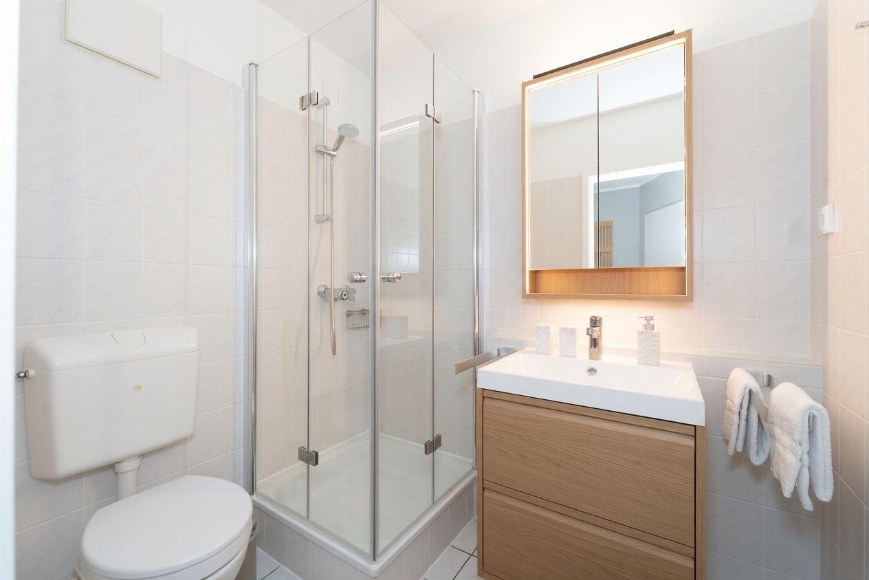 Badezimmer mit Dusche, Waschbecken und Toilette. Holzwaschtisch und Spiegelschrank.