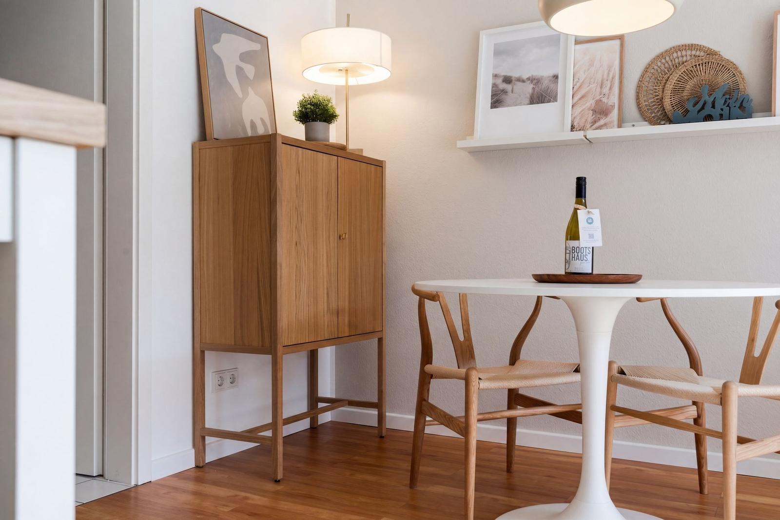 Esszimmer mit Tisch, Stühlen und Holzschränkchen. Wandregal mit Bildern und Dekoration.