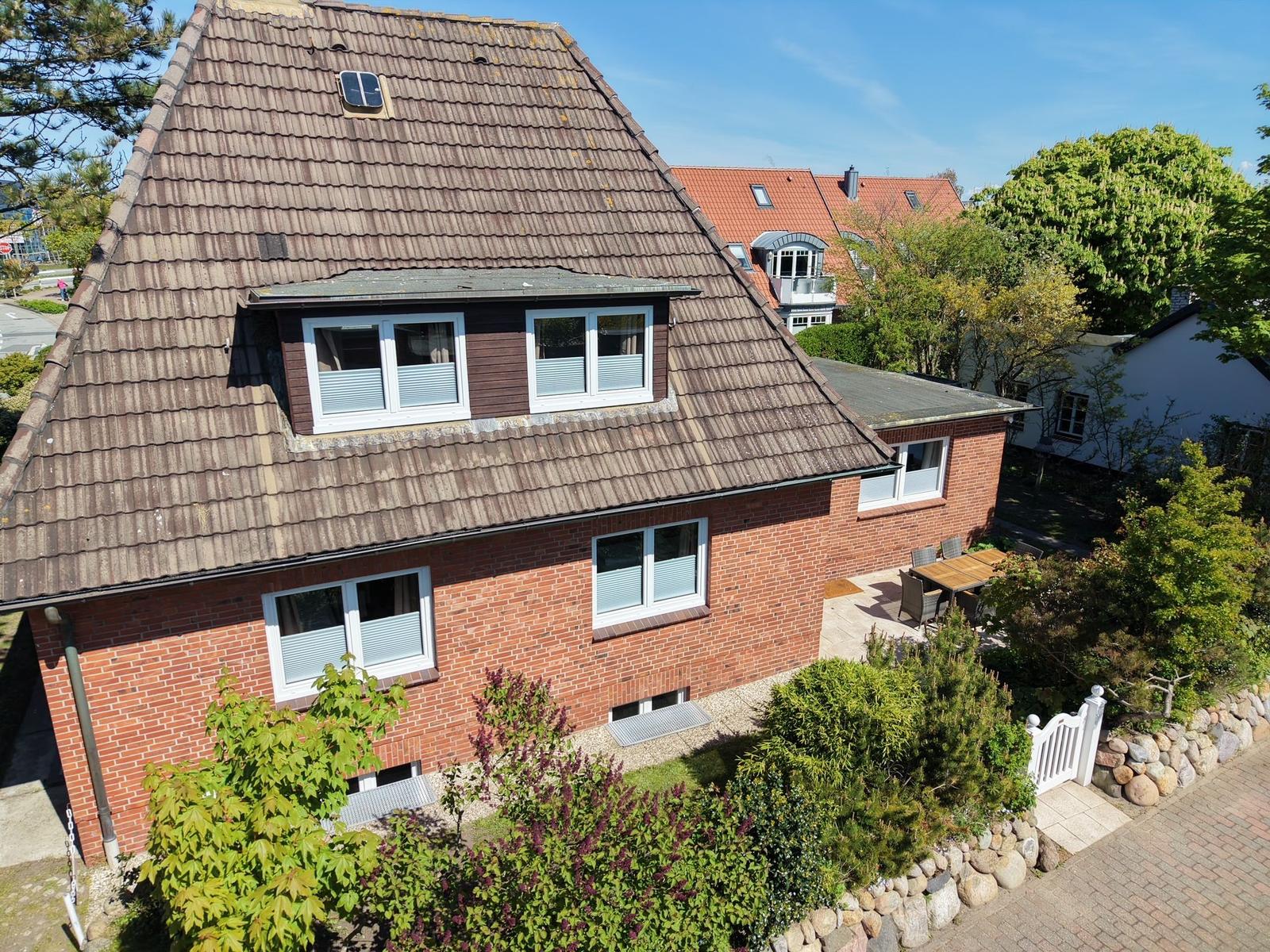 Ein zweistöckiges Haus mit braunem Dach und rotem Backsteinbau. Garten mit Tisch und Stühlen.
