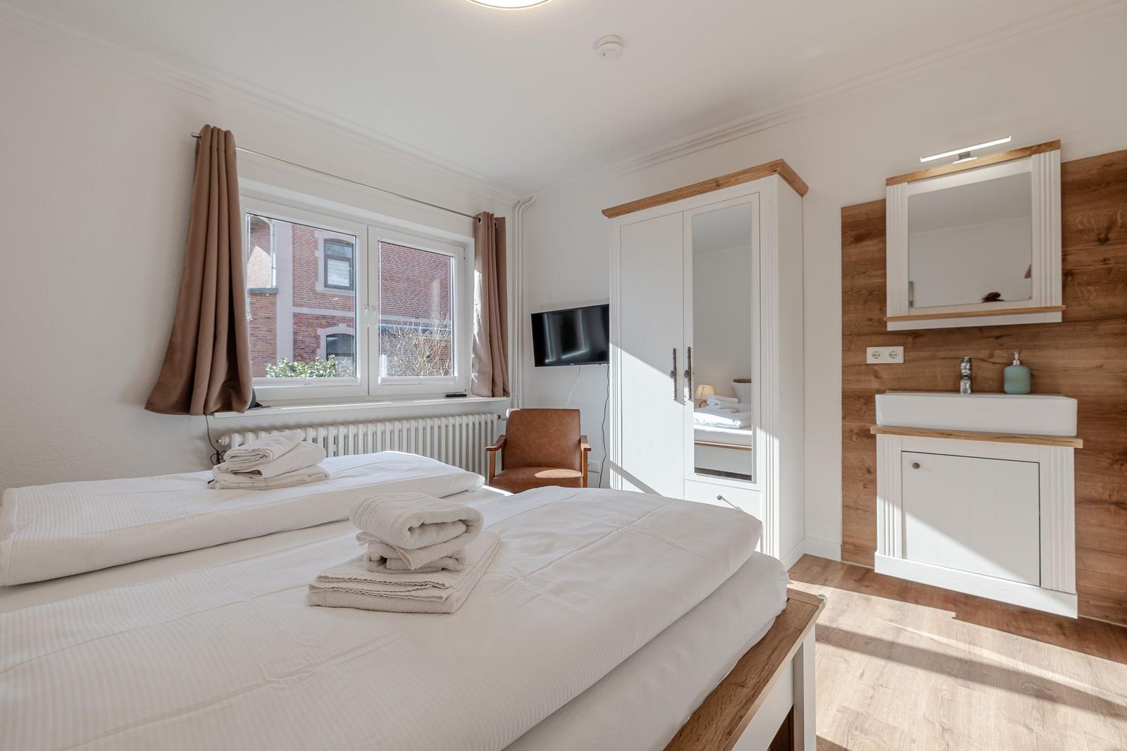 Schlafzimmer mit Doppelbett, Bad und Fenster. Holz- und weiße Möbel.