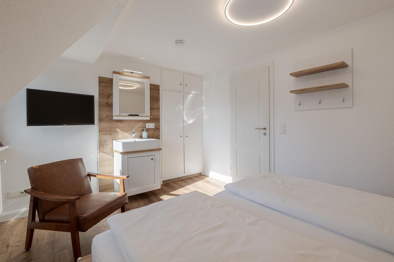 Schlafzimmer mit Bett, Schrank, Waschbecken und Fernseher an der Wand.