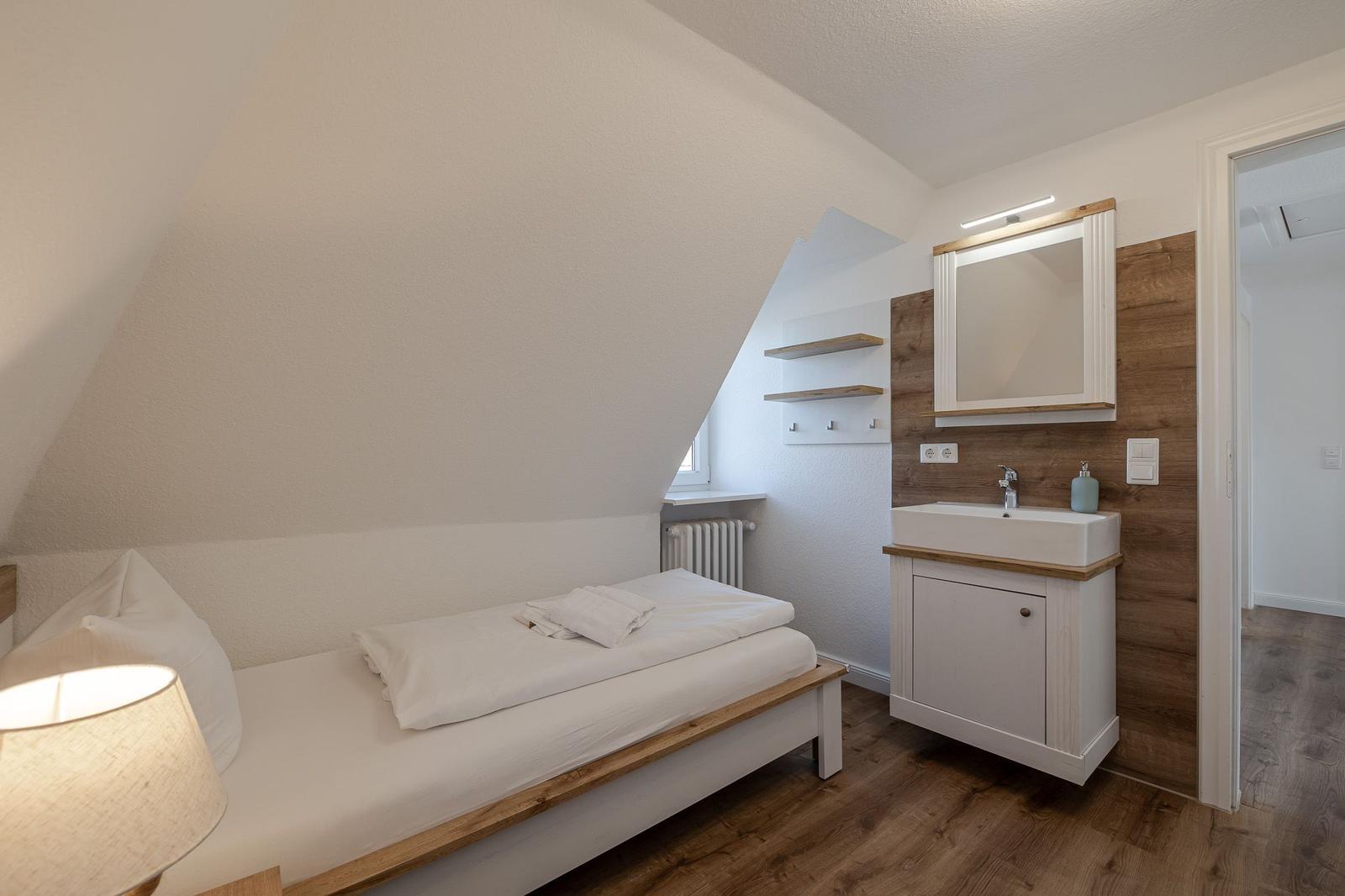 Schlafzimmer mit Dachschrägen, Bett, Waschbecken und Spiegel