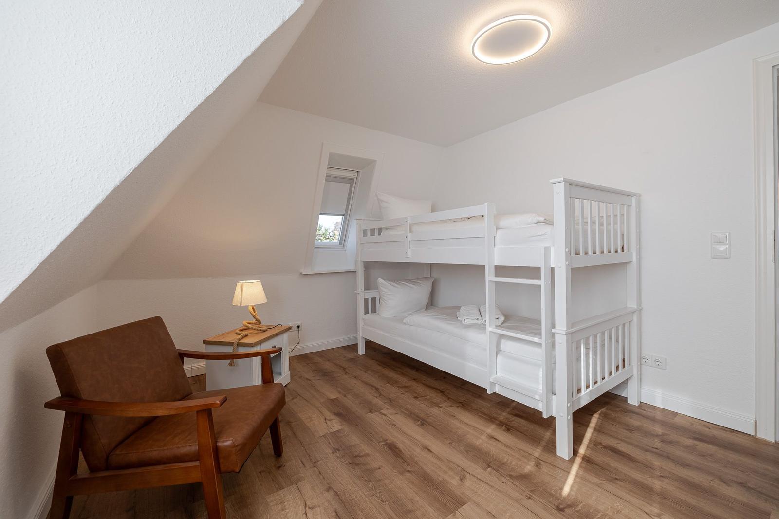 Schlafzimmer mit Doppelstockbett, Holzboden und Schreibtisch mit Lampe.