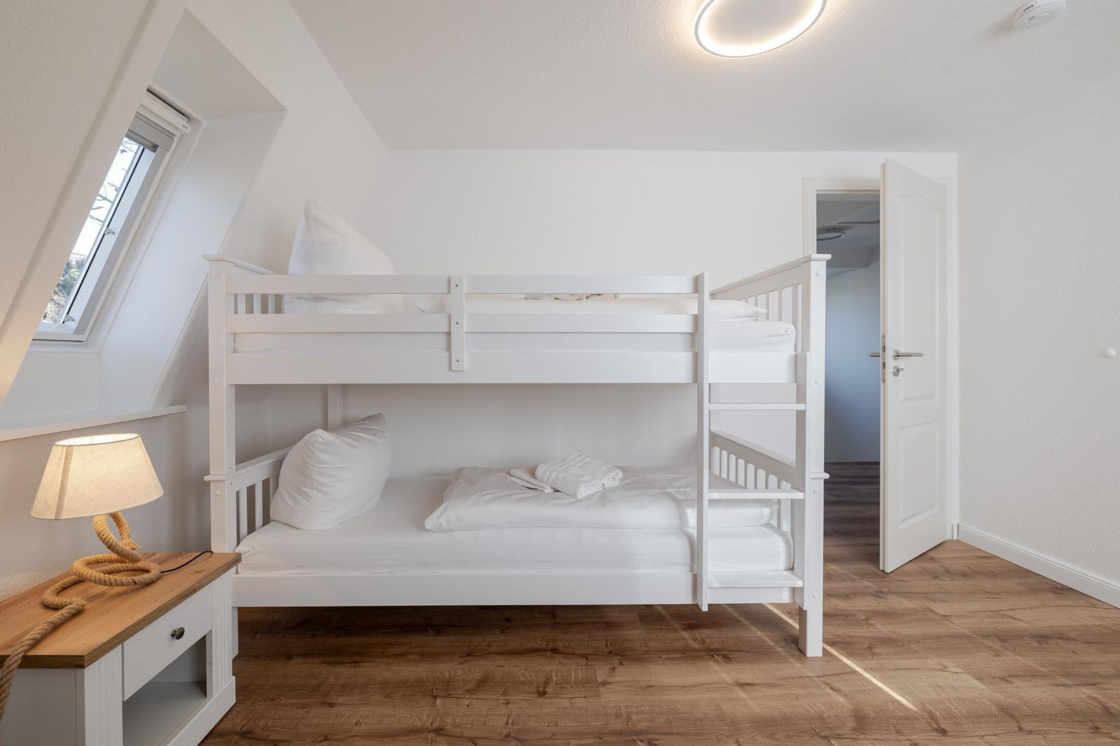 Zimmer mit Doppelstockbett, Holzboden und Dachfenster. Neben einem Schreibtisch mit Lampe.