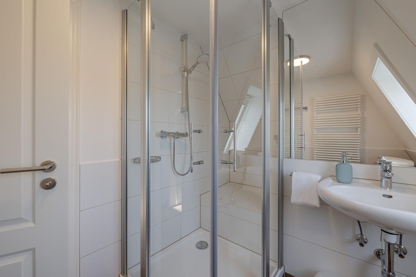 Duschkabine mit Duschbrause, Waschbecken und Spiegel im Badezimmer.