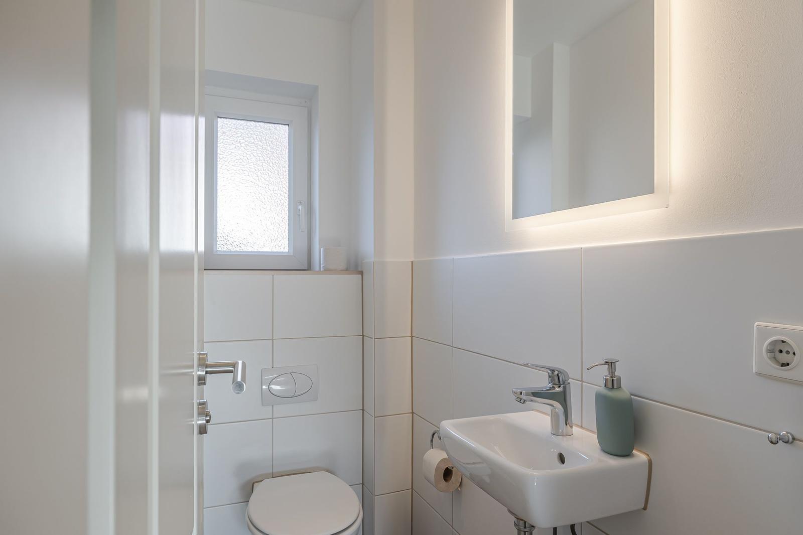 Badezimmer mit Toilette, Waschbecken und Spiegel mit Beleuchtung.