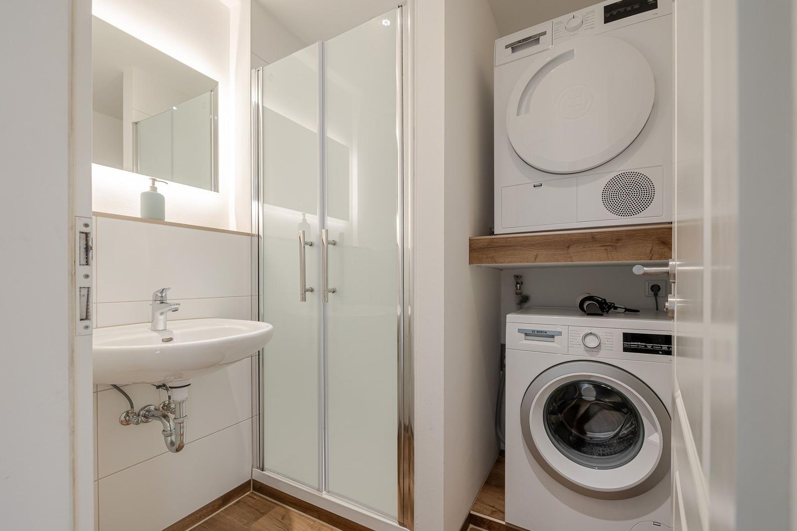 Badezimmer mit Dusche, Waschmaschine und Trockner.