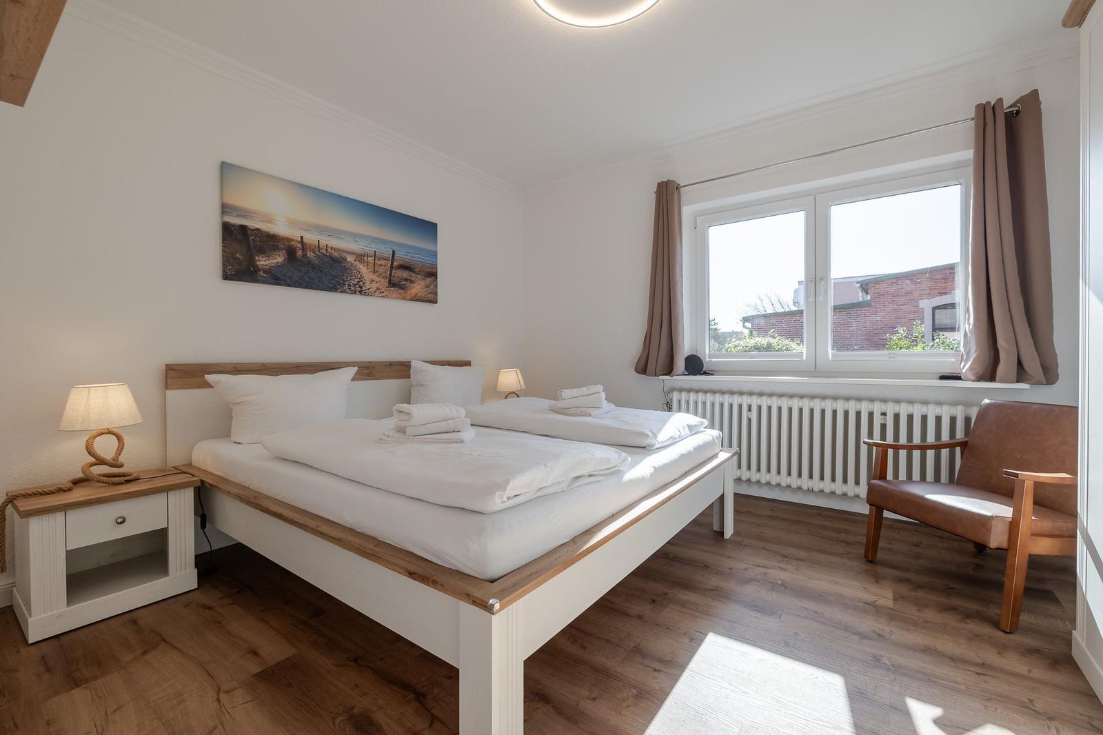 Schlafzimmer mit Doppelbett, Fenster, Stuhl und Wandbild.