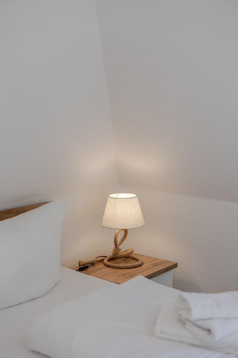 Schlafzimmer mit Bett, Nachttisch und Laterne aus Seil.