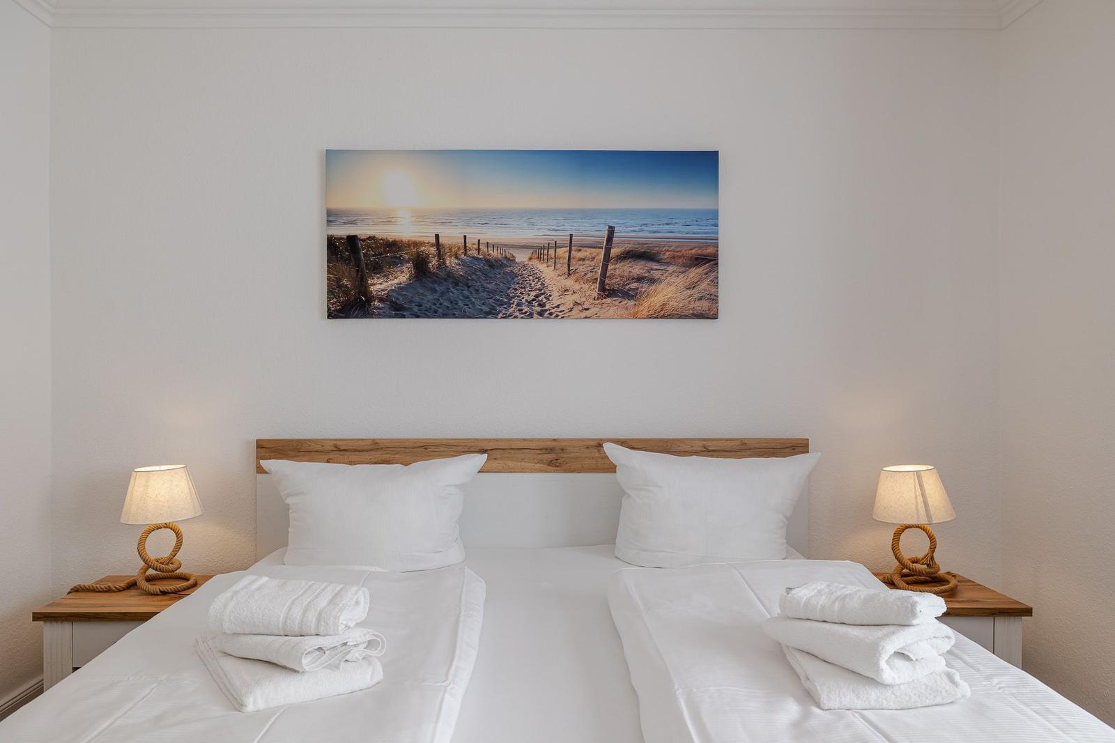 Schlafzimmer mit Doppelbett, zwei Nachttischen und Strandbild an der Wand.