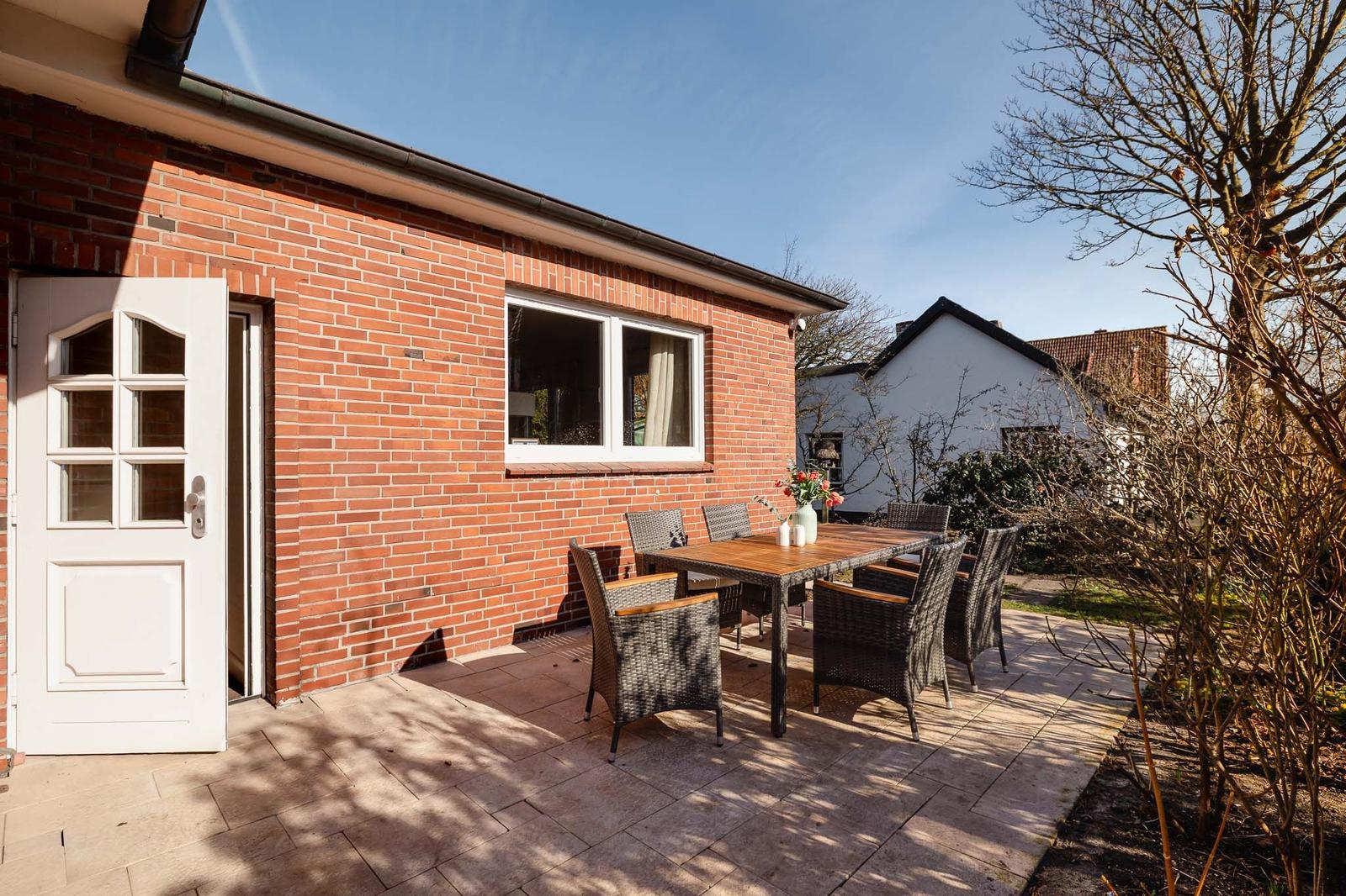 Terrasse mit Tisch und Stühlen neben rotem Backsteinhaus mit weißen Fenstern und Tür.