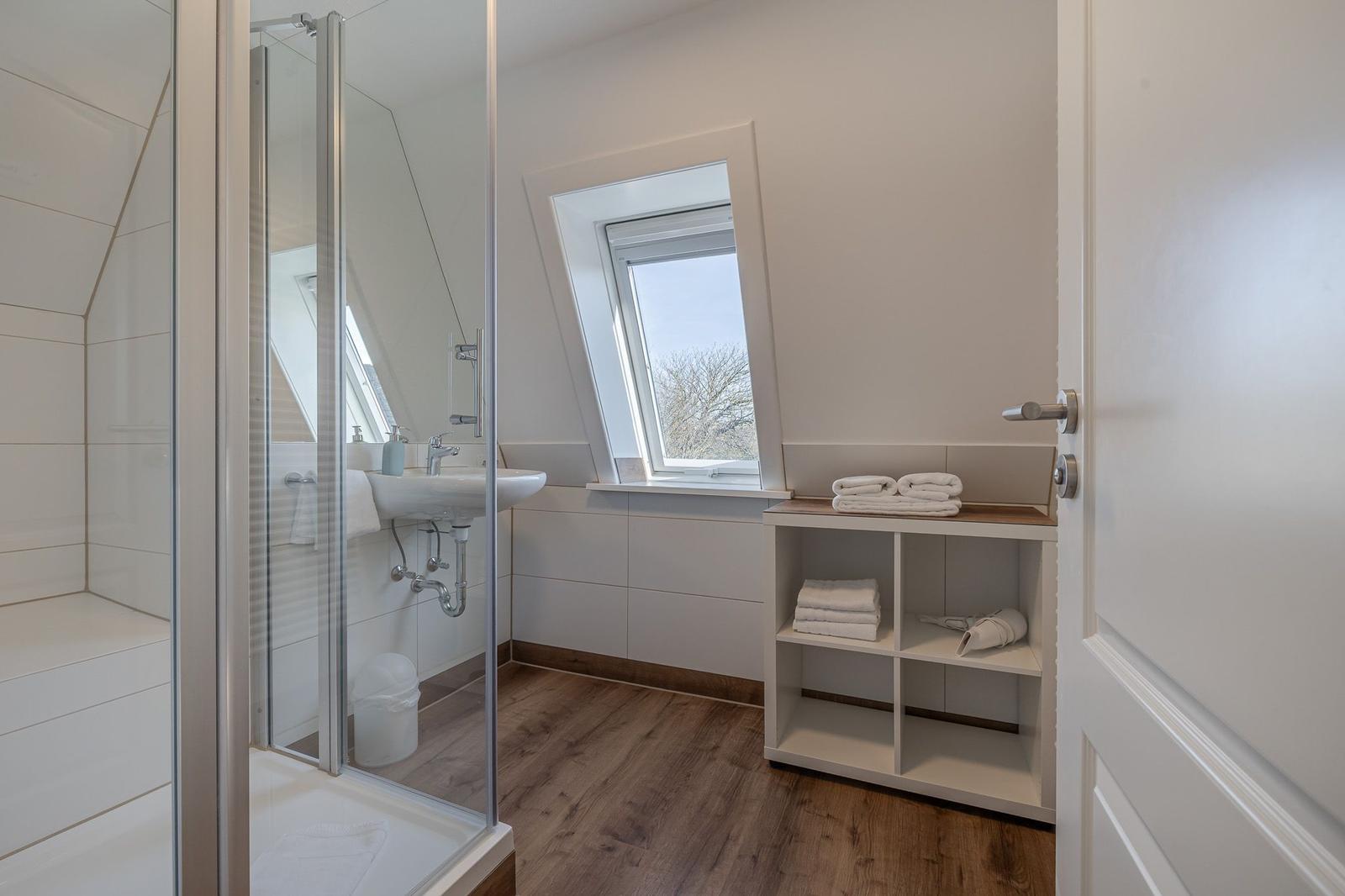 Badezimmer mit Dusche, Waschbecken und Dachfenster. Handtücher und Regal sind vorhanden.