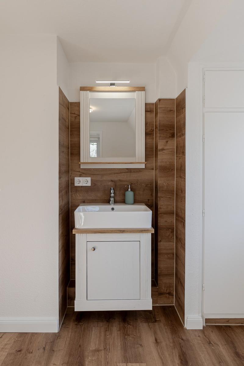 Badezimmer mit Waschbecken, Spiegel und Holzwandverkleidung.