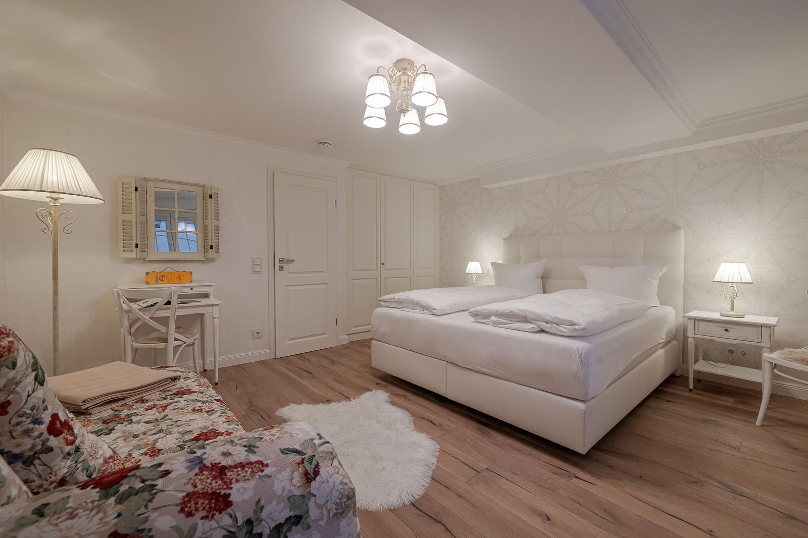 Schlafzimmer mit weißem Bett, Holzboden und Schreibtisch mit Spiegel.