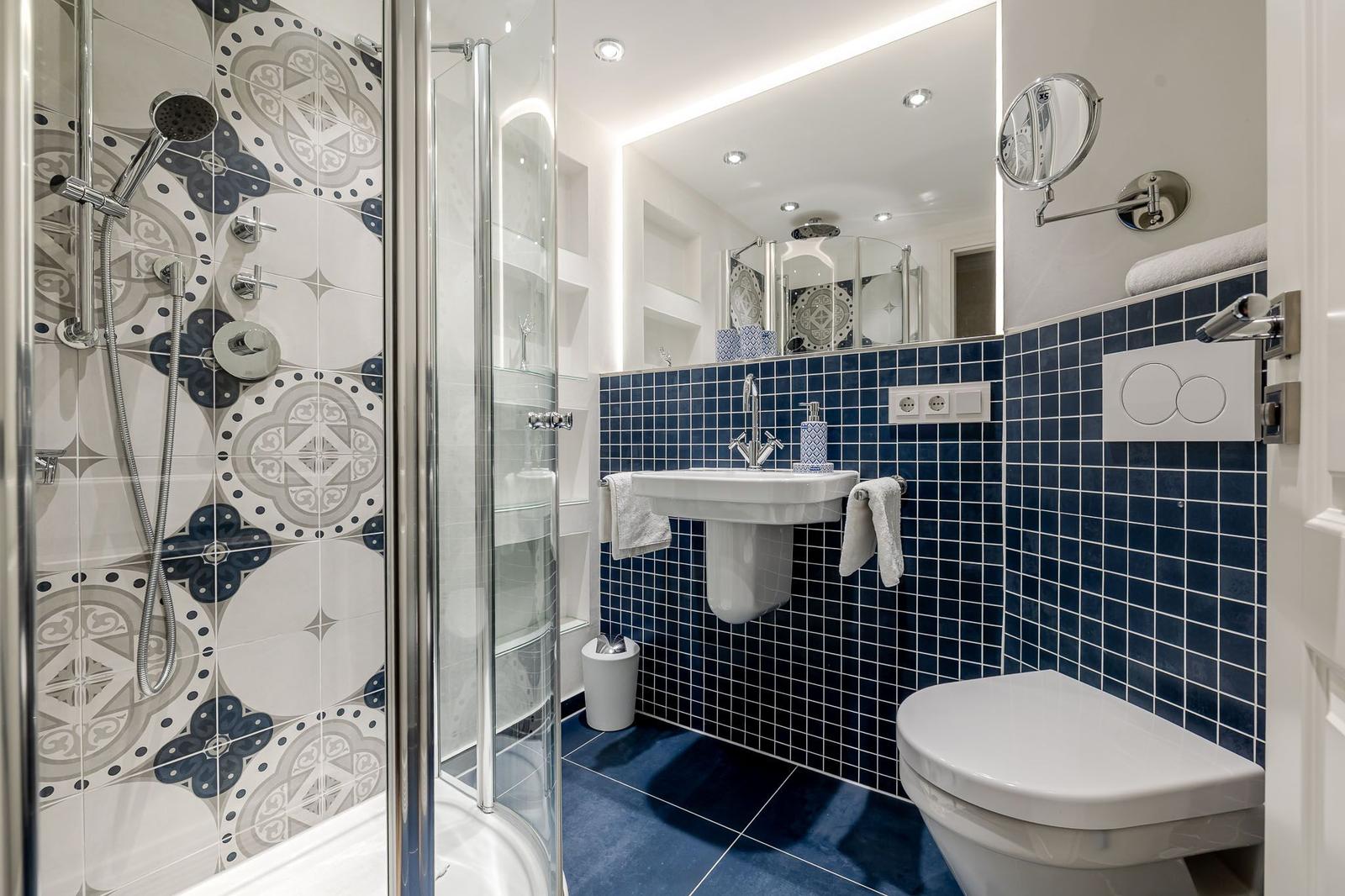 Badezimmer mit Dusche, Waschbecken und Toilette. Wandfliesen in Blau und Muster.