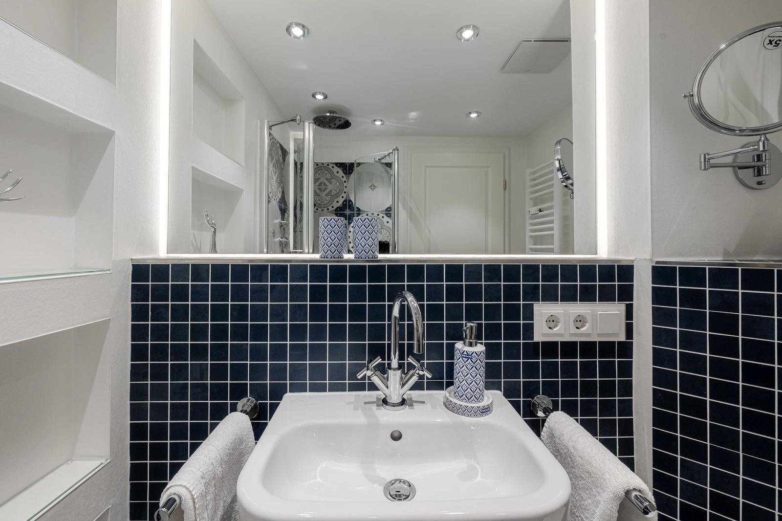 Badezimmer mit Waschbecken, Spiegel und Dusche. Wandfliesen in Blau und Weiß.