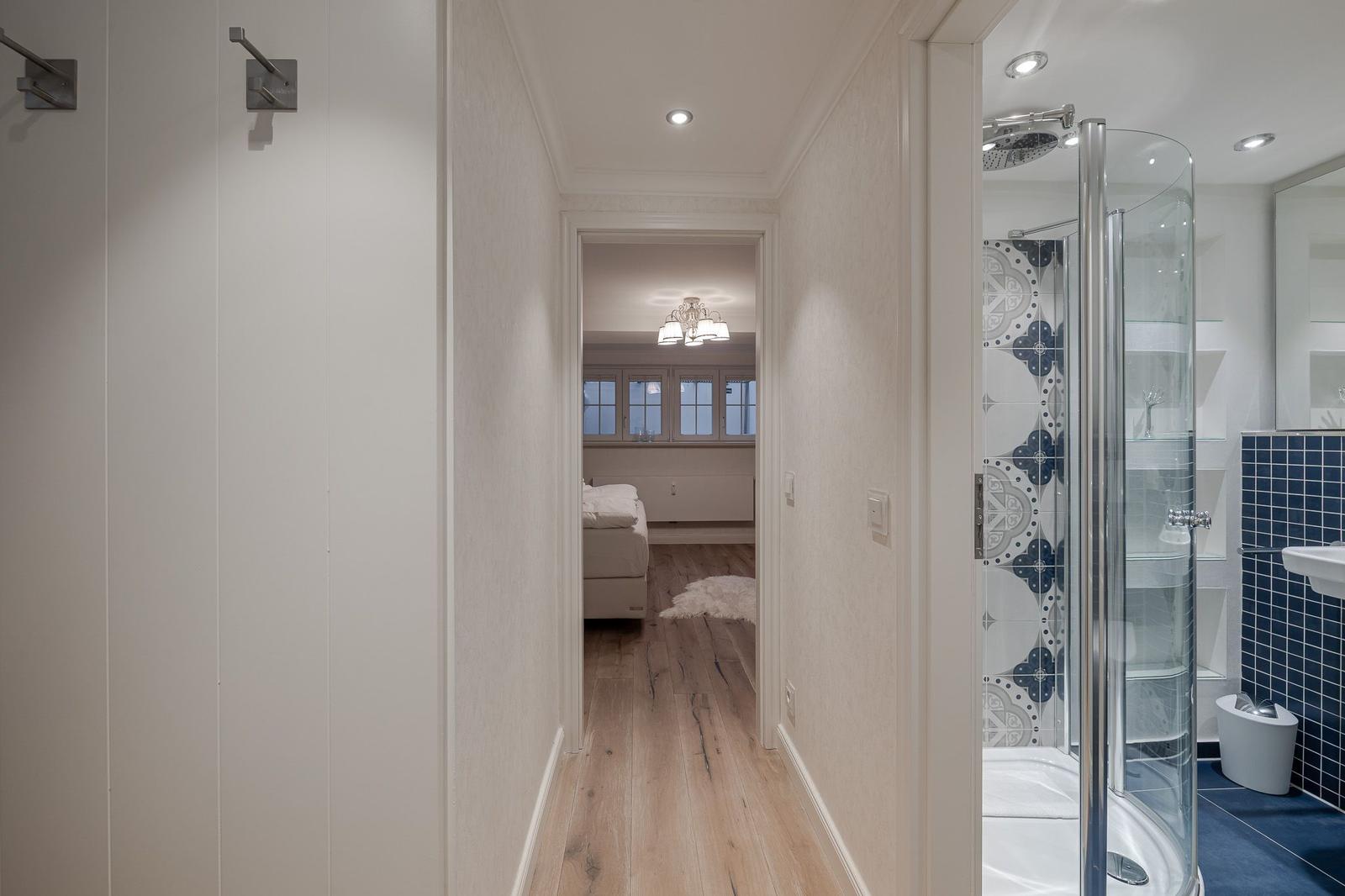 Flur mit Schlafzimmer und Dusche. Holzboden, weiße Wände und Glasdusche.