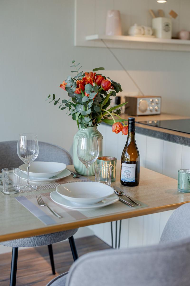 Esstisch mit Platz für zwei, Blumen, Wein und Geschirr.