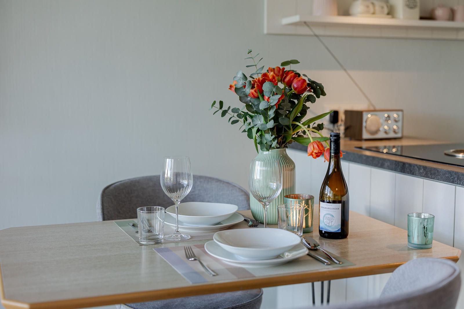 Esstisch mit Platz für zwei, Blumenvase und Weinflasche.
