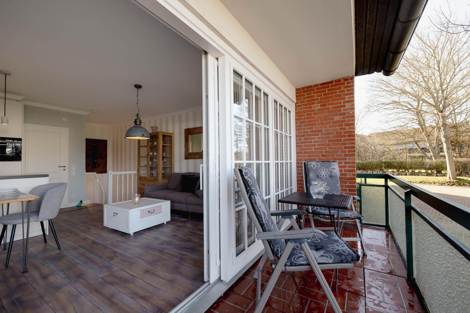 Terrasse mit Tisch und Stühlen, Blick ins Wohnzimmer mit Sofa und Küchenbereich.